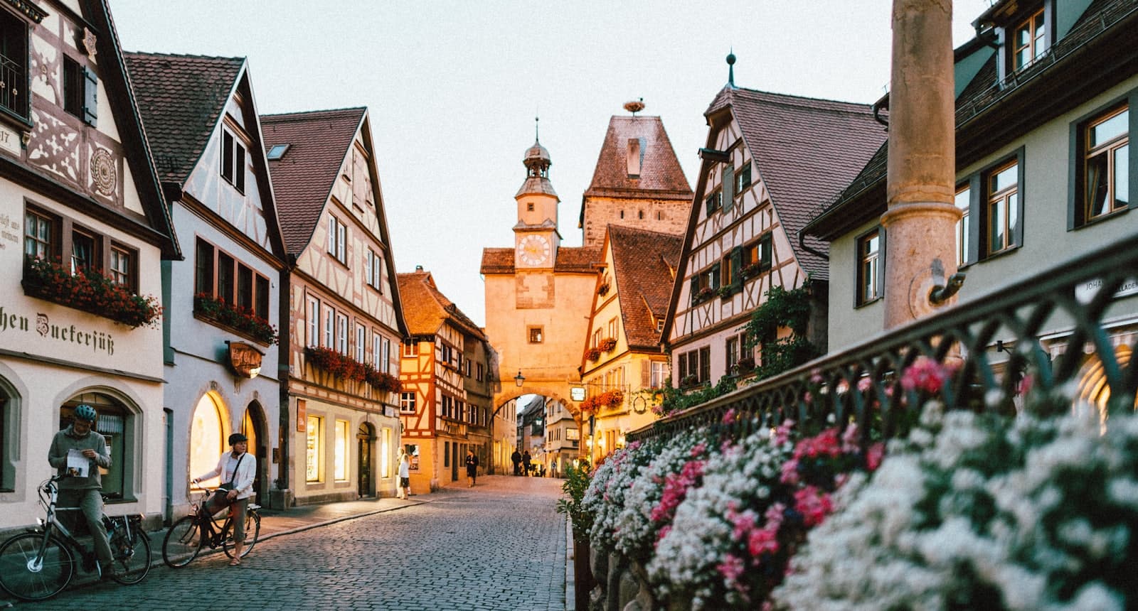 A bustling medieval trade town at golden hour, its lanes lined with merchant houses.