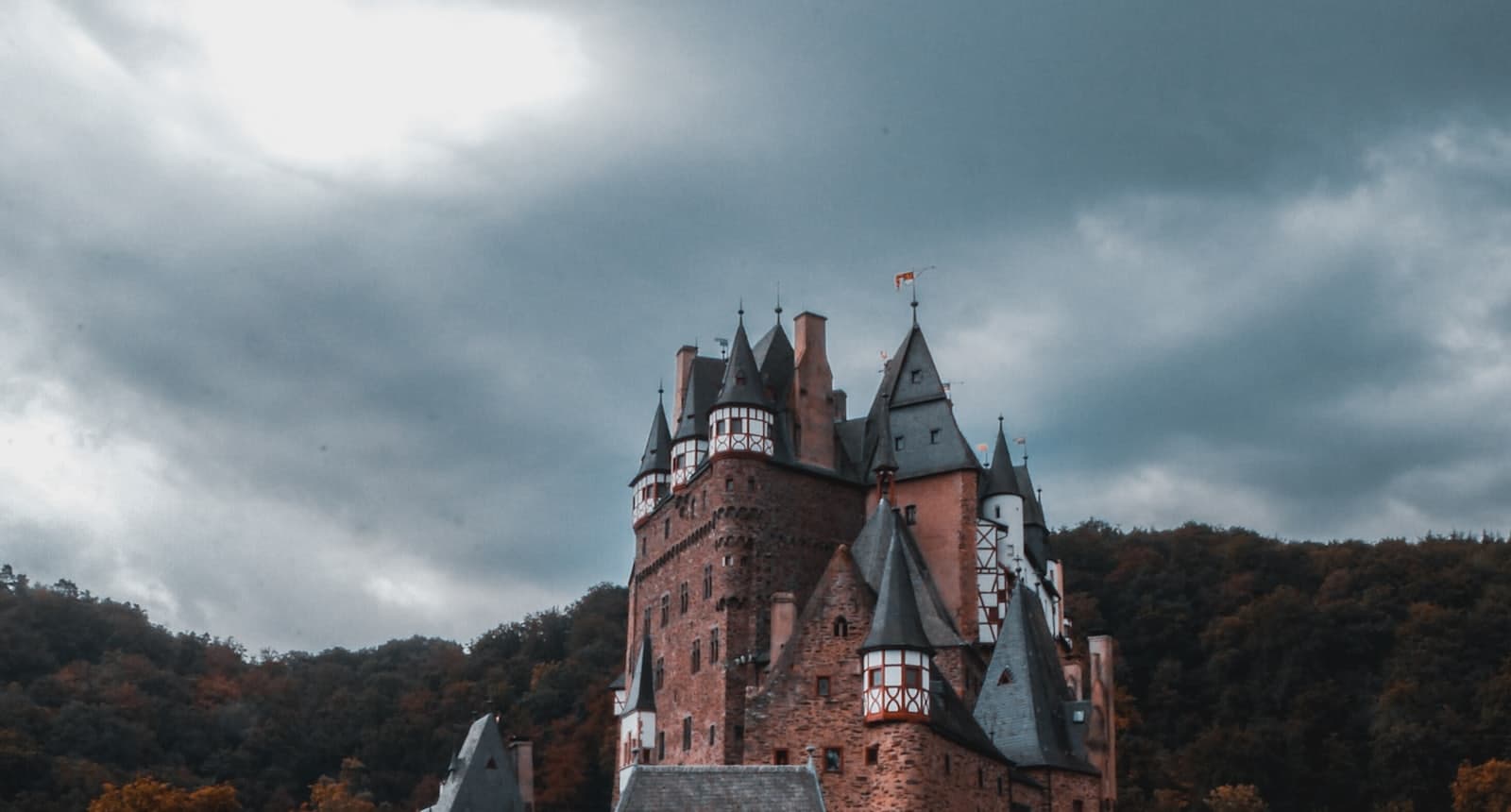 A fortified medieval castle crowning a forested ridge beneath a brooding sky.