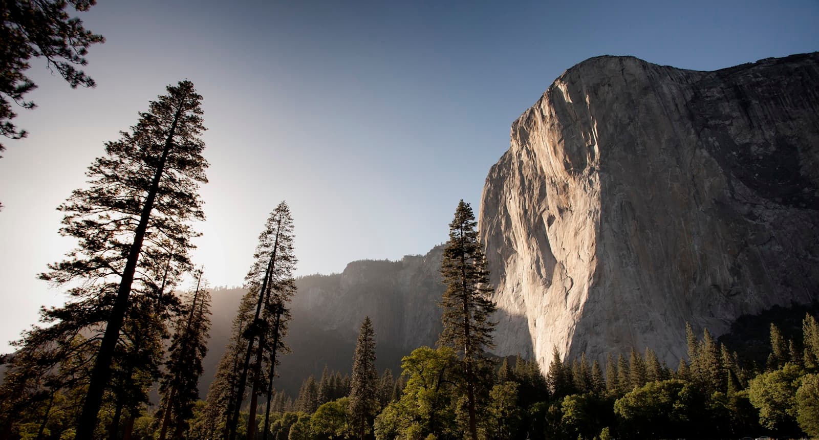 Sunlit wilderness of cliffs, forests, and open meadow at the frontier's edge.